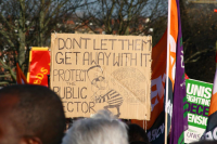 Public sector workers during a strike. The photo displays a placard saying "don't let them get away with it, protect public sector"