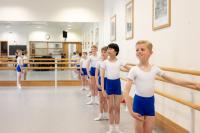 Child dancers standing in line holding a barre