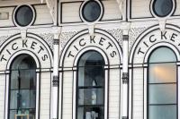 Exterior of a ticket office. A black and white building with three windows that have the word 'tickets' printed over