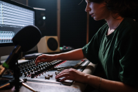 A woman in a green t-shirt working a a studio mixing desk