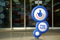 Blue National Lottery sign, showing its crossed fingers logo, in front of shop entrance.