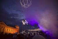 Man hangs from trapeze in outdoor festival performance at night