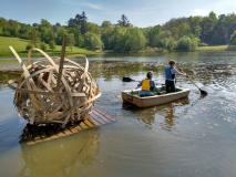 Photo of people in rowing boat towing a wooden sculpture