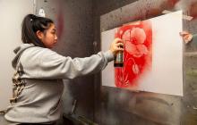A girl spray painting a poppy onto a wall using a stencil