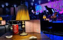 A table in the foreground with a lamp, menu and 'I have been sanitised' marker with a band on stage in the background