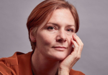Headshot of Natalie Melton, Executive Director at Crafts Council. She has ginger hair and wears an orange top. Her hand rests on her face. She looks at the camera, smiling slightly.