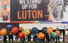 Revoluton picture of people carrying cooured umbrellas in front of building with mural 'We stand up for Luton'