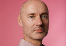 Jan De Schynkel, Rosetta Arts Chief Executive. He is a bald, white man wearing a shirt, photographed against a pink background.