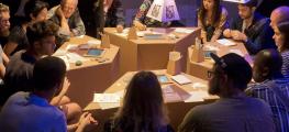 Photo of an interactive installation, a group of people meet around cardboard tables