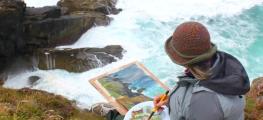 A person sitting at the edge of a cliff painting a picture of waves crashing against rocks below
