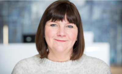 Former Head of Visual Arts at Creative Scotland Amanda Catto. She has a fringe and brown hair, wears a grey jumper and smiles at the camera. The background is blurred.