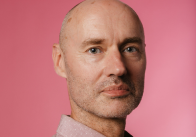 Jan De Schynkel, Rosetta Arts Chief Executive. He is a bald, white man wearing a shirt, photographed against a pink background.