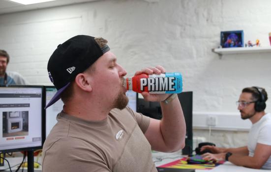 Young man sitting in an office drinking from a bottle branded 'Prim