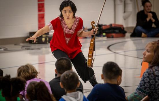Woman with violin teaching young children in a school hall