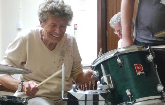 An older woman playing a drum kit