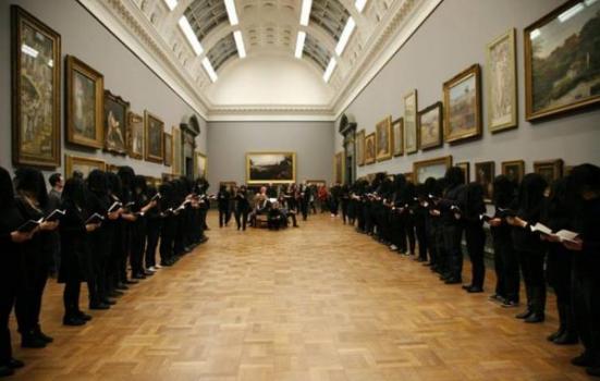 People dressed in black stand in large gallery