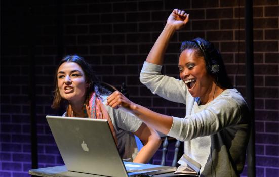 Photo of two women, one is celebrating with here hand in the air in front of a macbook