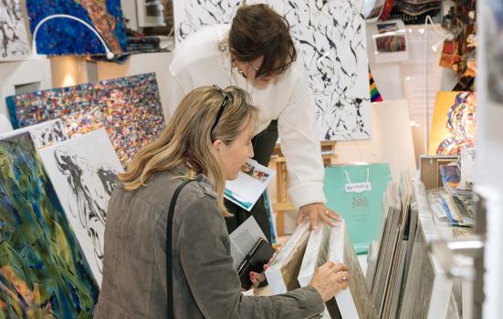 two women flicking through painting canvasses in a studio or shop setting