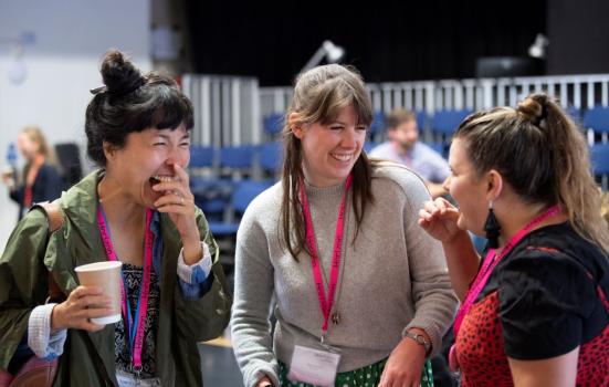 Artists and delegates networking. Image depicts three people stood together at a work event laughing.