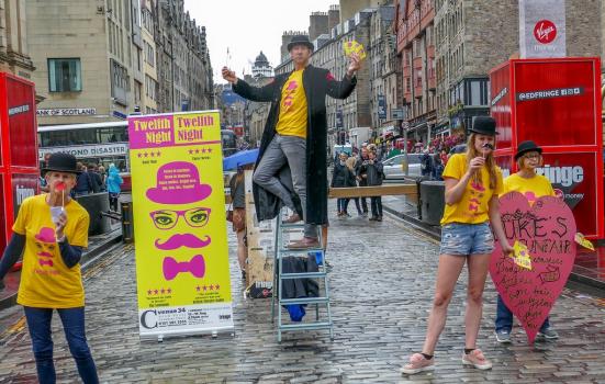 People standing next to a street billboard at the Edinburgh Fringe Festival