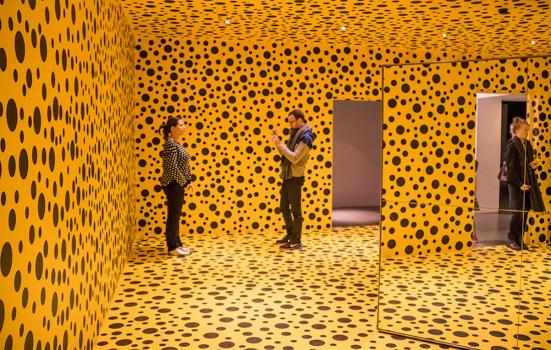 three people standing in an all-yellow room with black spots painted on the walls, ceiling and floor