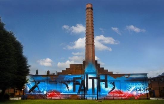 A building with a tall tower and a wall covered in a bright mural saying 'faith'