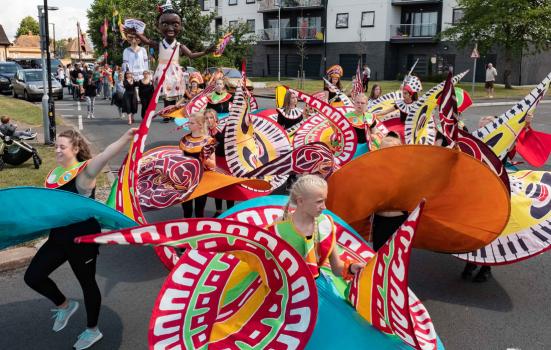 Carnival dancers parading through Tilbury, Thurrock adorned in brightly coloured garments accented with a keyboard pattern