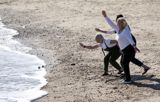 Photo of three woman skimming stones on a beach