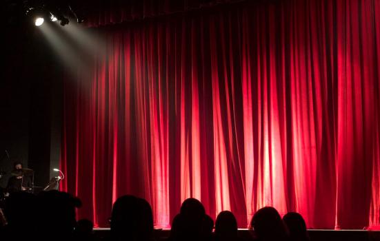 Photo of a silhouette of an audience facing a red stage curtain