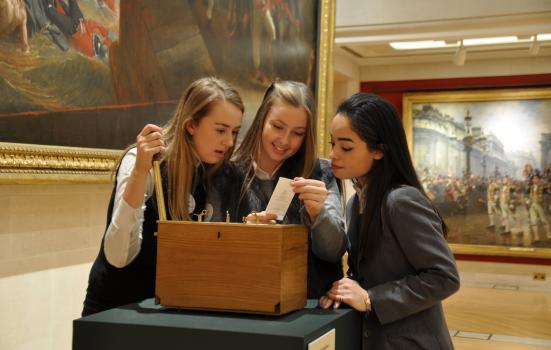 Photo of three girls in gallery standing over a box