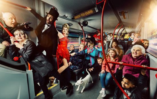 'Back to Ours' company photo. A diverse range of people photographed from the inside of a bus. There are people sat down and stood up. Some are performing, others are smiling and gasping.