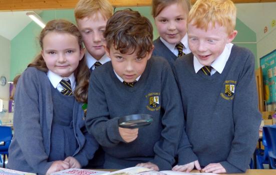 Photo of schoolchildren looking at books with microscope