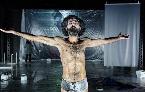 Photo of a bearded actor, clad only in stained briefs, arms outstretched