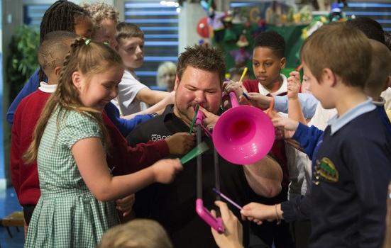 Photo of musician with pink trombone surrounded by school children
