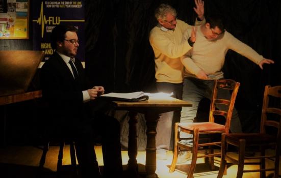 Photo of three men rehearsing a play round a table