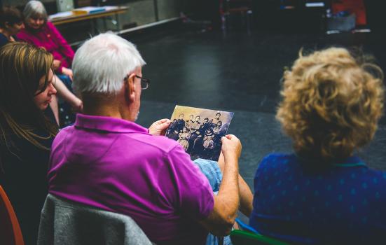 photo over the shoulder of an older gentleman sitting down who is looking at a photograph