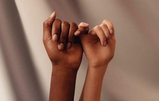 A close up two female hands, one black one white, locked in a "pinky promise" gesture