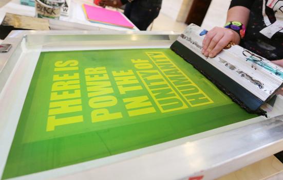 screenprinting a poster which says "There is power in the unity of humanity"