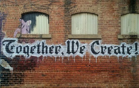 Graffiti on a brick wall reading 'Together We Create'