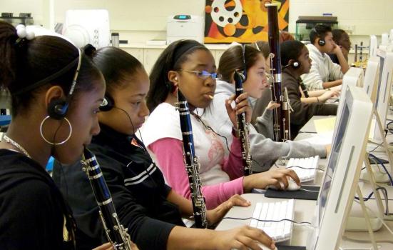 Young people with clarinets recording music on desktop computers