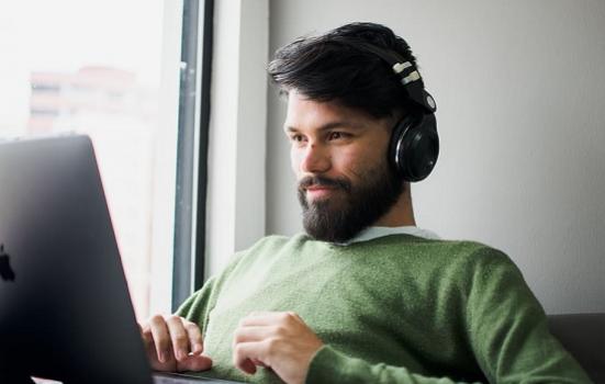 A man sitting with a macbook on his lap while wearing headphones