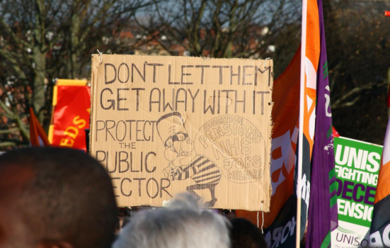 Public sector workers during a strike. The photo displays a placard saying "don't let them get away with it, protect public sector"