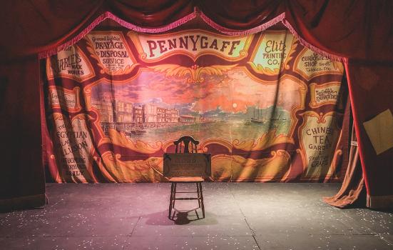 Empty stage with a period backdrop with the word 'Pennygaff' in the background and a chair in the foreground with a 'closed' sign on top