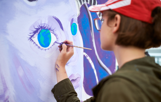 Female painter draws picture with paintbrush on canvas for outdoor street exhibition