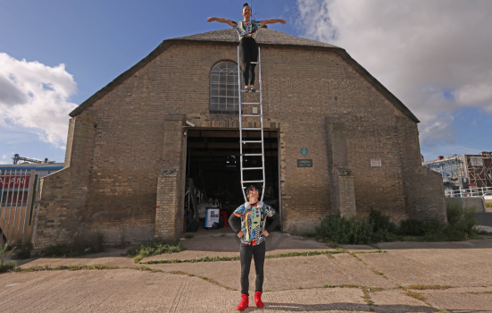 A circus performer balances on top of a ladder in front of the Ice House in Great Yarmouth