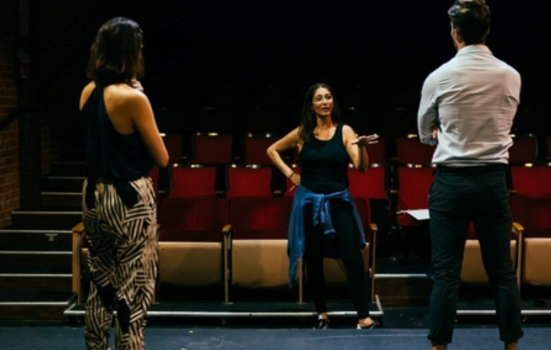 Female director giving feedback on a scene to two actors in a theatre by