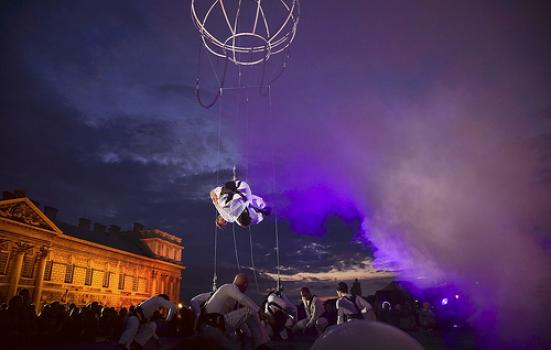 Man hangs from trapeze in outdoor festival performance at night