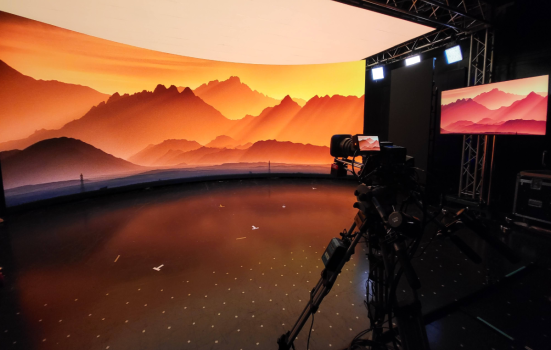 an example of virtual production technology. a projector displays a virtual image of a sunset and is being recorded by a video camera. to the right of the picture, a computer displays the same image
