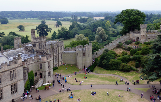 Exterior of part of Warwick Castle. The photo is an aerial view of the castle walls, showing members of the public in the castle grounds