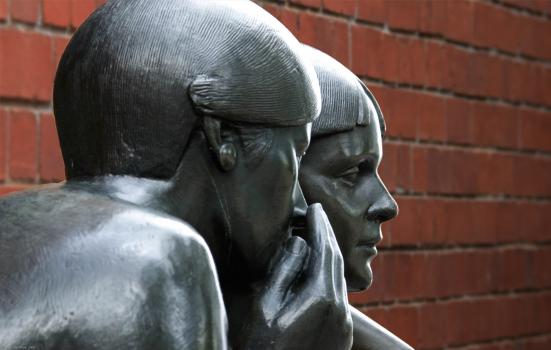A photo of a statue of a person whispering into someone's ear